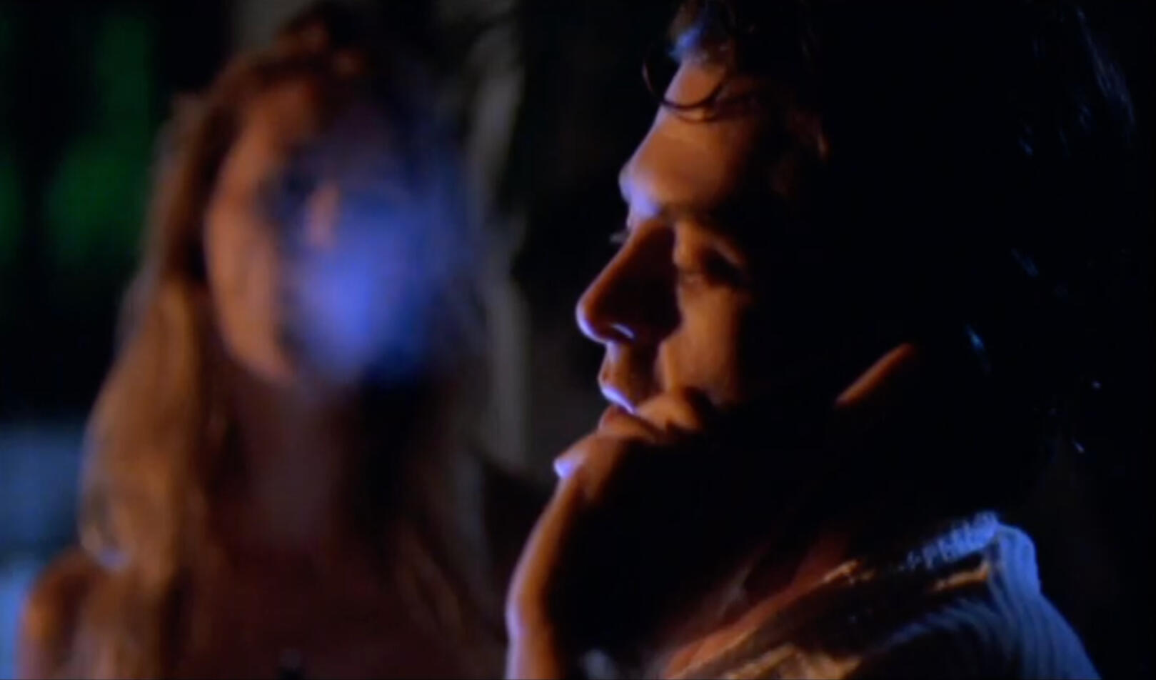 Image of a woman blowing smoke, out-of-focus in background with foreground image of profile o man on phone