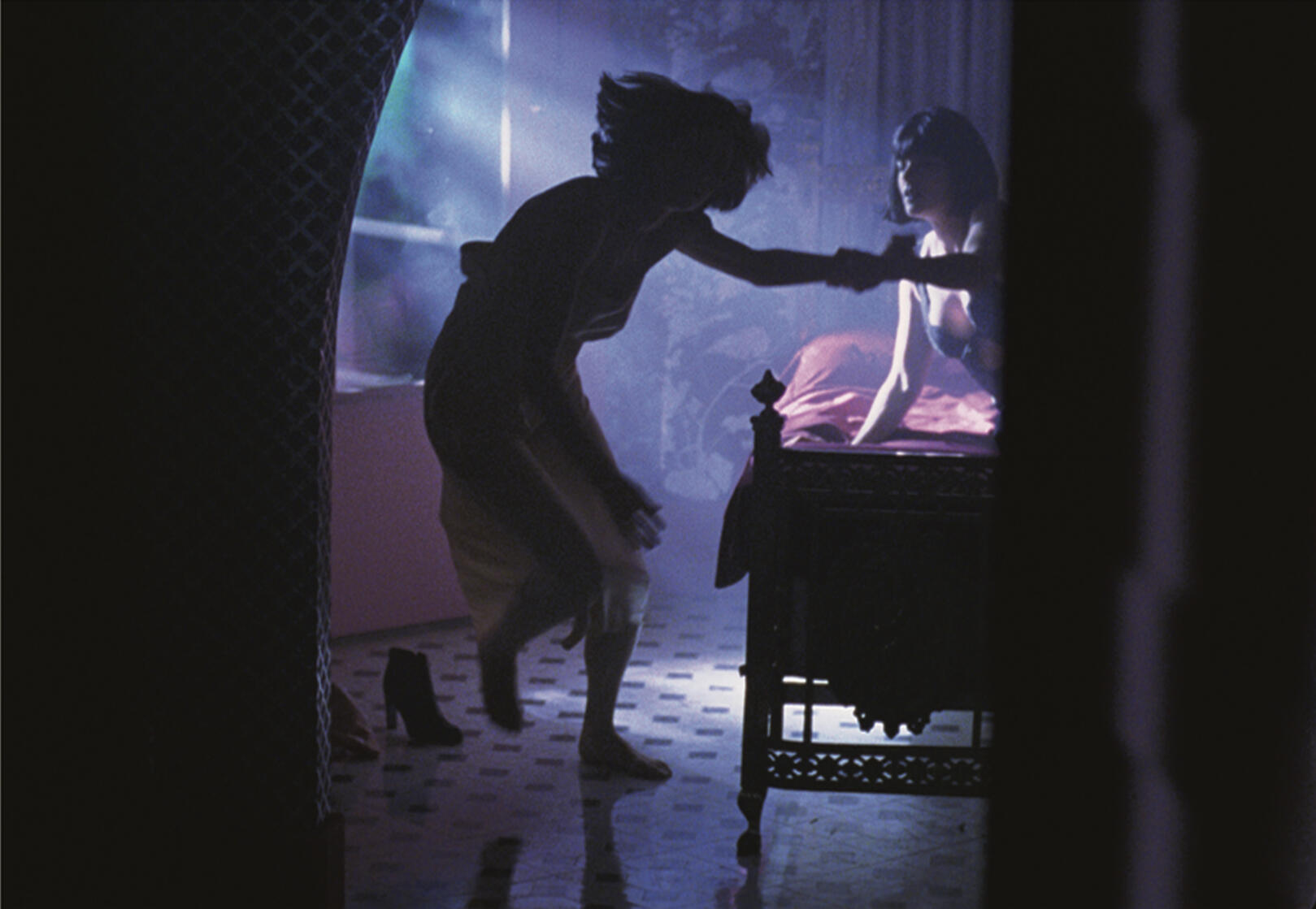 Nightmare scene with back and side lighting of woman in bed reaching out to a woman running away