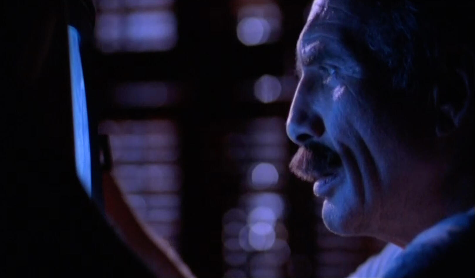 Edge lit image of man's face in profile looking into a monitor in cool tones