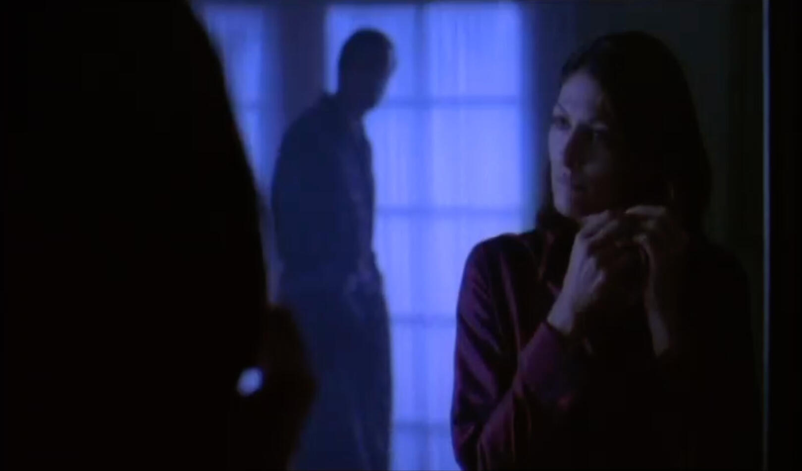 Image of bedroom interior with dramatic lighting of a woman looking into a mirror and limited Depth of Field with the silhouette of a man in front of a woman
