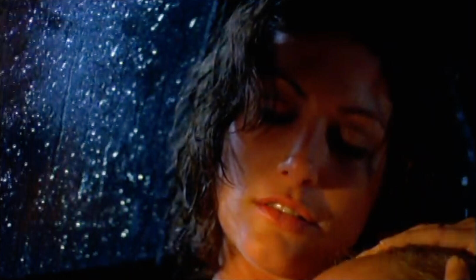 Car interior portrait of warm lit woman's face at night, rain on windshield